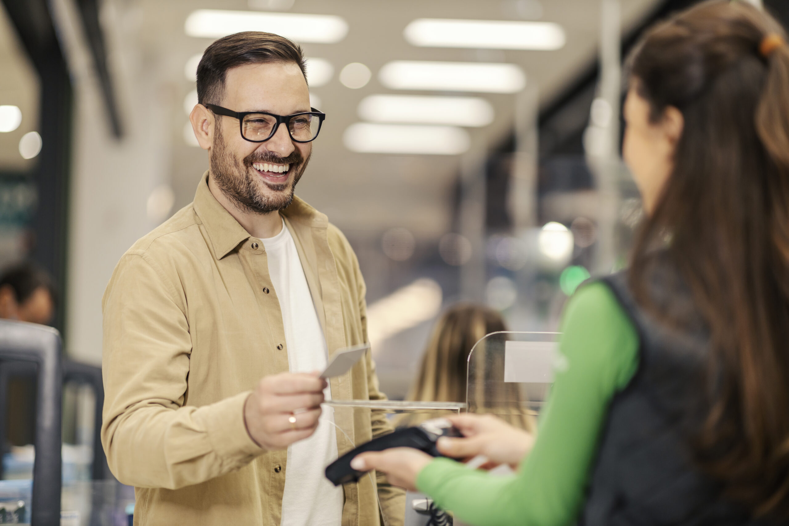 A smiling man is purchasing with credit card on pos terminal at checkout.